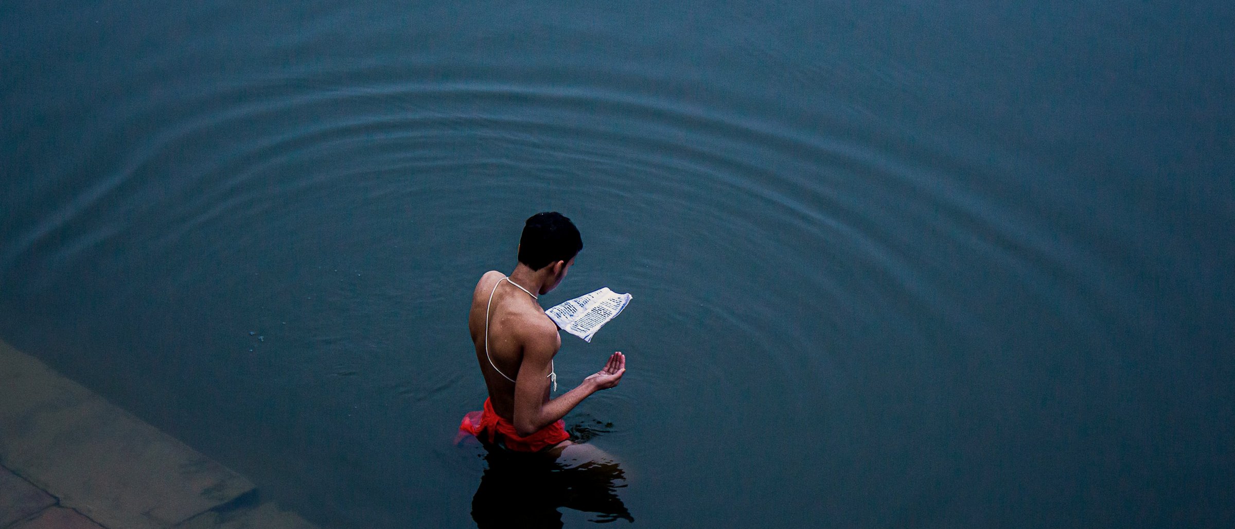 A man standing in the river, reciting from a text